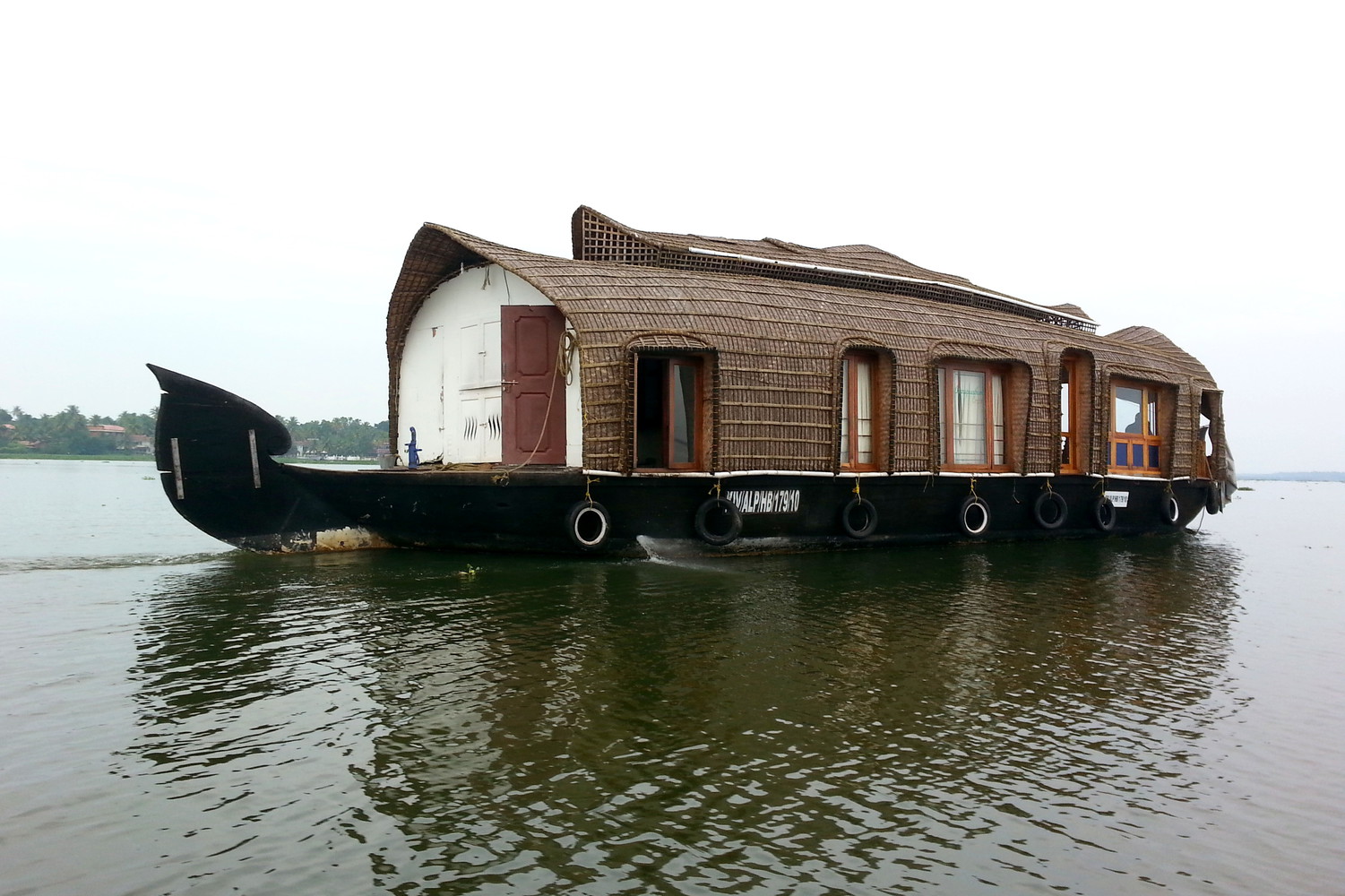A houseboat with large wooden windows floating on the backwaters