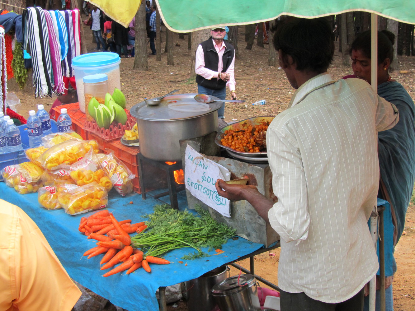 A vendor selling carrots, soup, mangoes, and other food on a food cart