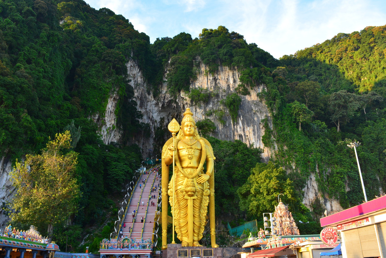 A tall statue of Lord Murugan in front of a flight of stairs leading to limestone caves named Batu Caves