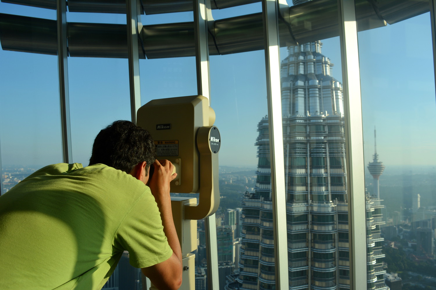 A guy using binoculars to watch the top portion of one tower from another tower