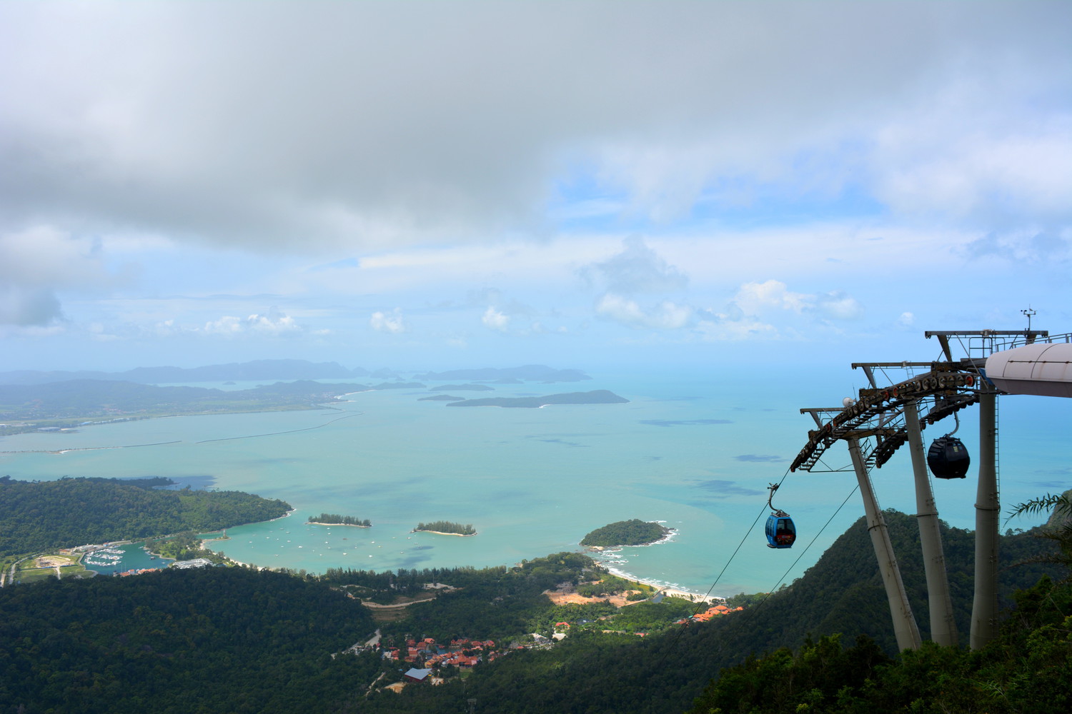 A panaromic view of hills, sea, islands in the sea, and a cable car station from the top of a mountain