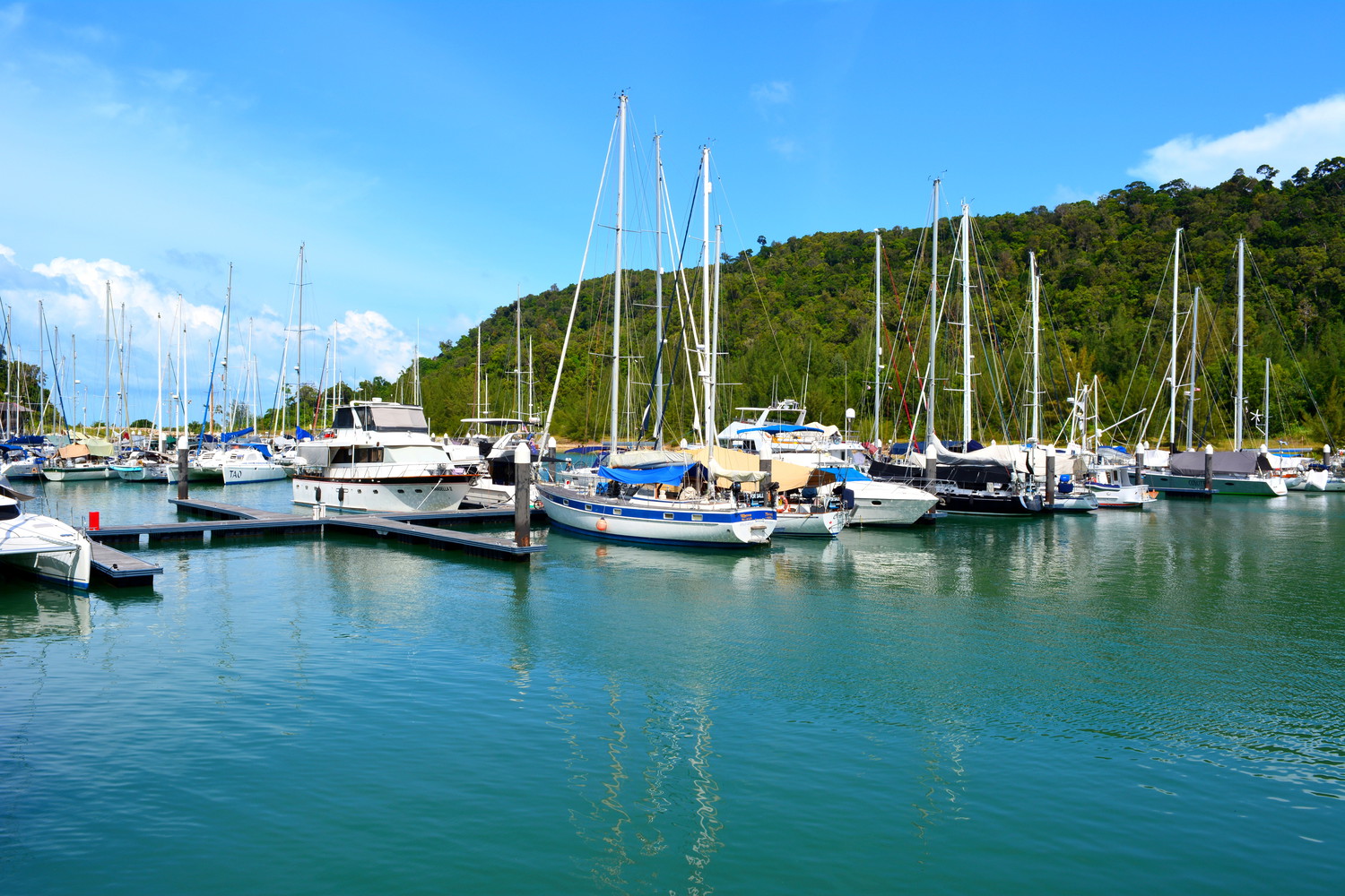 Boats docked at the Strait of Malacca with hills covered with trees visible behind