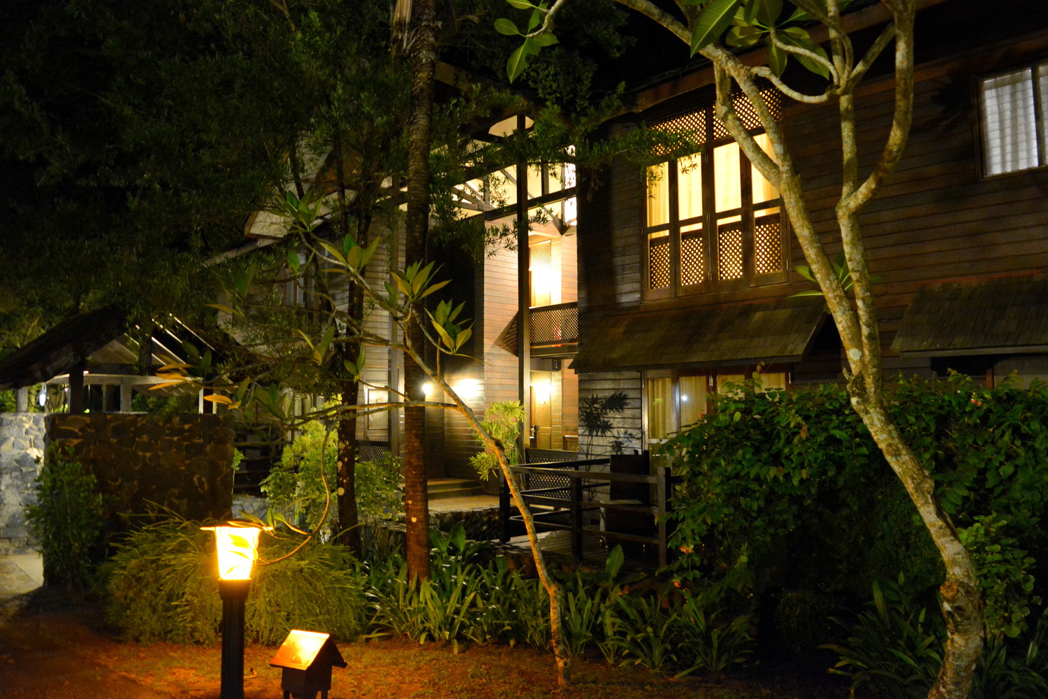 A two storey hotel building made of wood surrounded by trees and shrubs low height orange lights