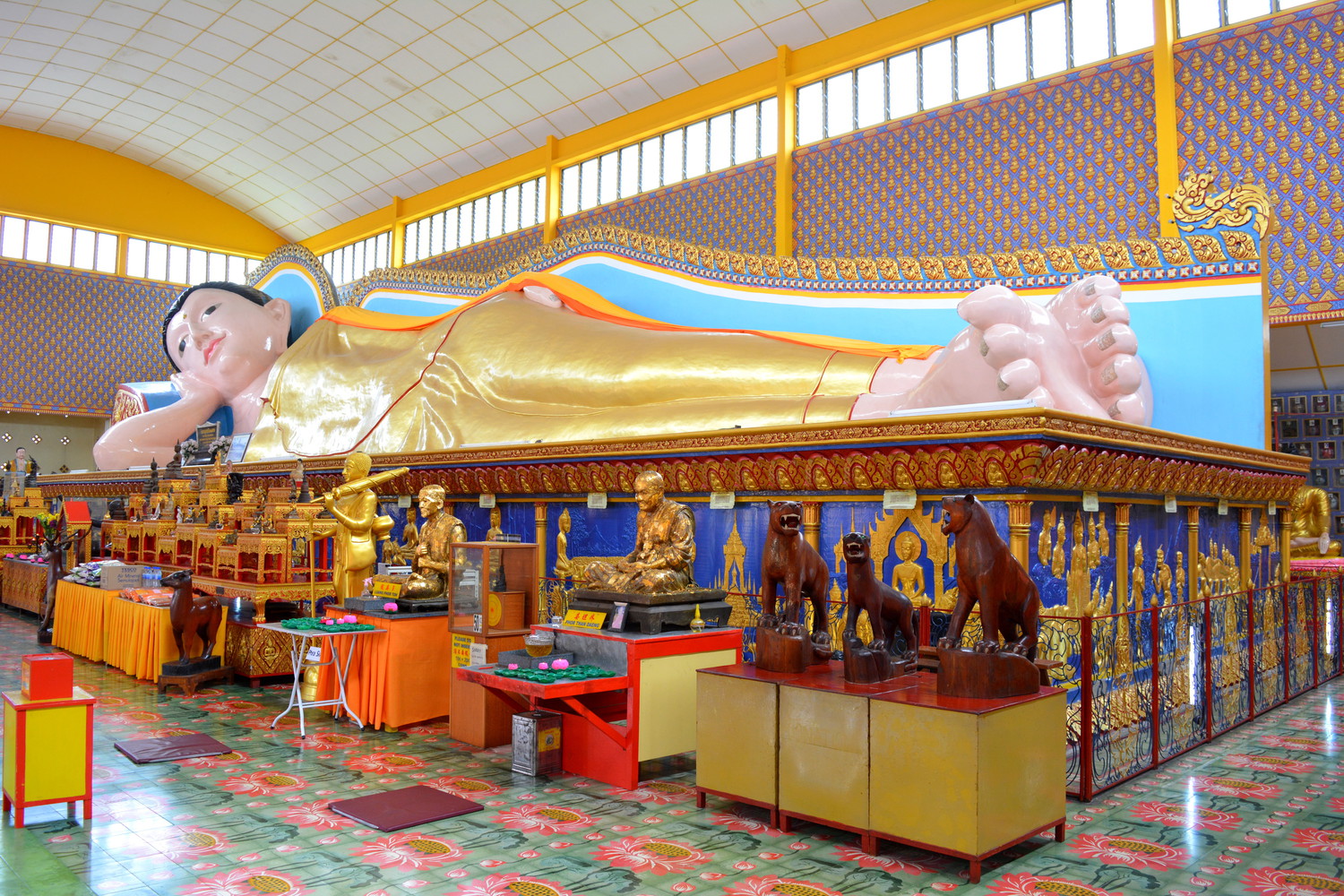 A massive statue of reclining Buddha with many smaller statues in front of it inside a temple