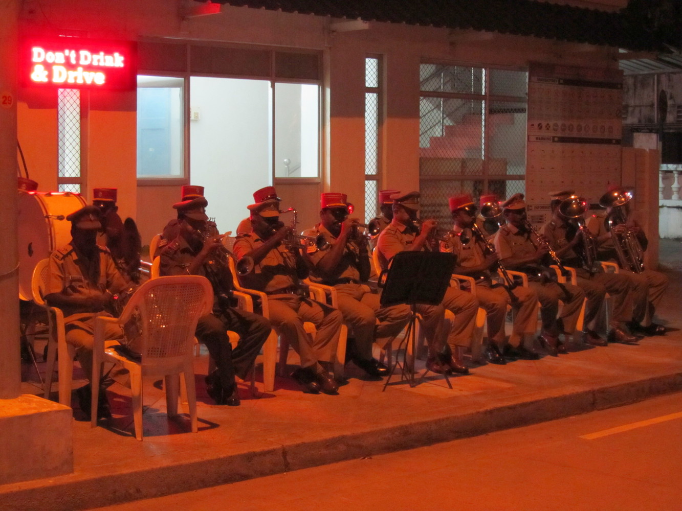 Cops in uniform sitting on chairs on a pavement and playing musical instruments such as drum and trumpets