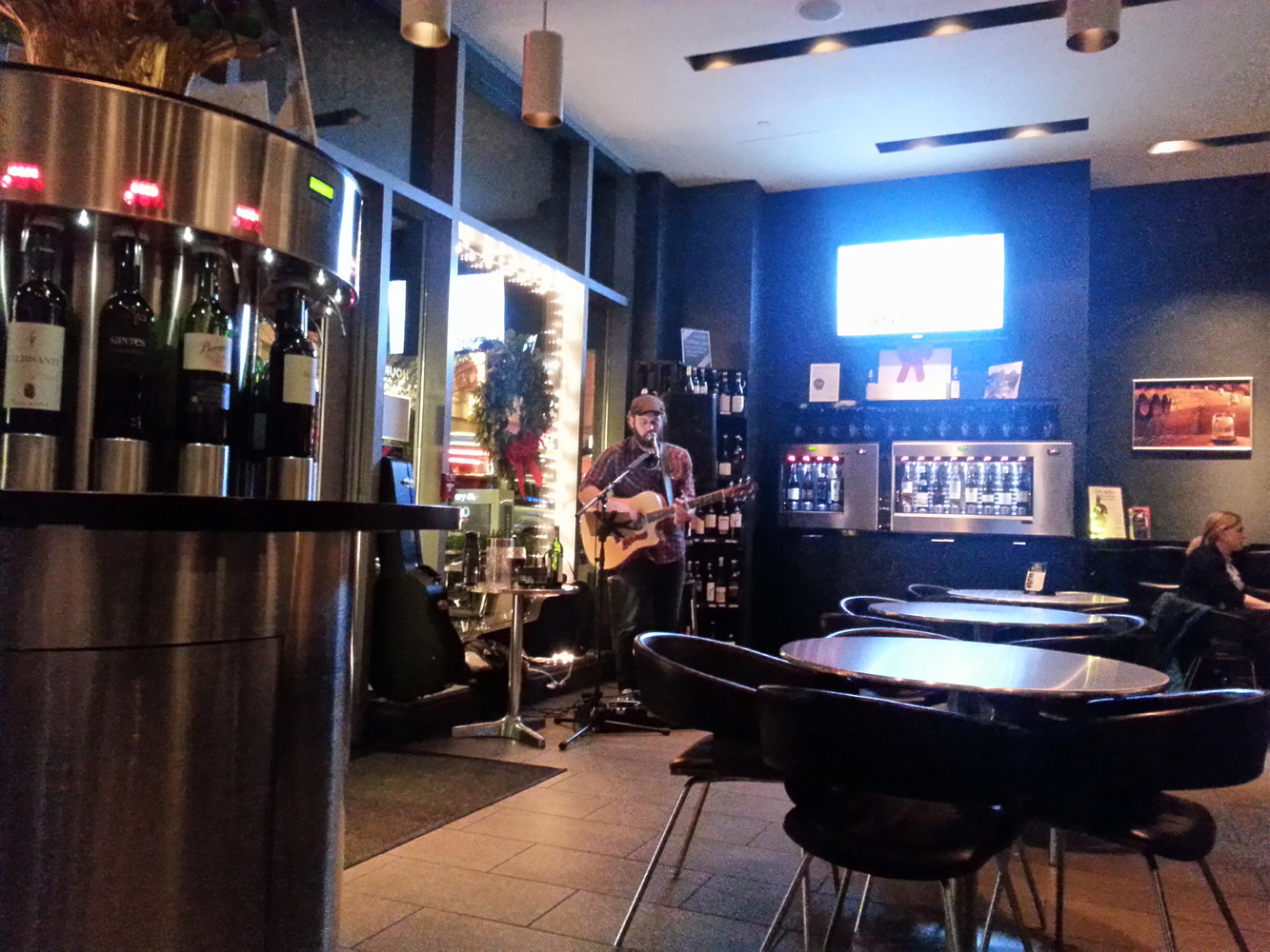 The interior of a restaurant with wine bottles stacked in shelves and a guitarist performing live music